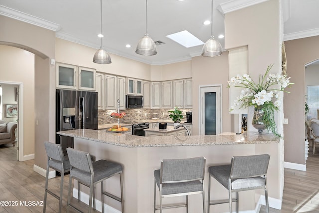 kitchen featuring tasteful backsplash, light wood-type flooring, a breakfast bar area, arched walkways, and appliances with stainless steel finishes