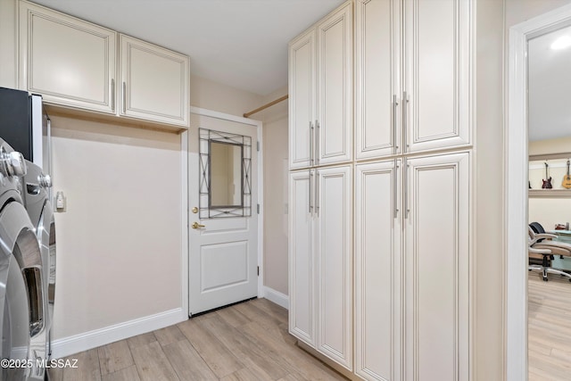 clothes washing area featuring cabinet space, light wood-style floors, washing machine and clothes dryer, and baseboards