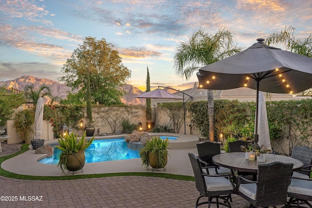 pool at dusk with a fenced backyard, a patio, an in ground hot tub, and a mountain view