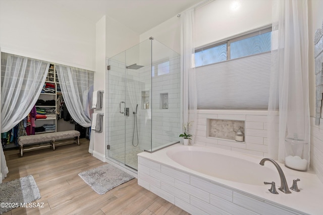 full bath featuring wood finished floors, a stall shower, a spacious closet, and a bath