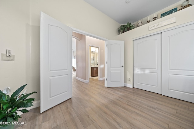 unfurnished bedroom featuring arched walkways, a closet, light wood finished floors, and baseboards