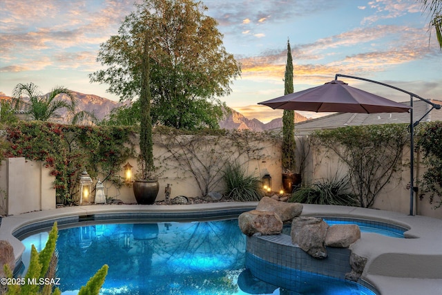 pool at dusk featuring a fenced in pool, a fenced backyard, and a mountain view