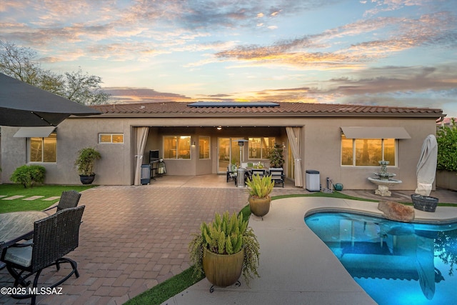 back of house at dusk with stucco siding, a patio, roof mounted solar panels, outdoor dining area, and a tiled roof