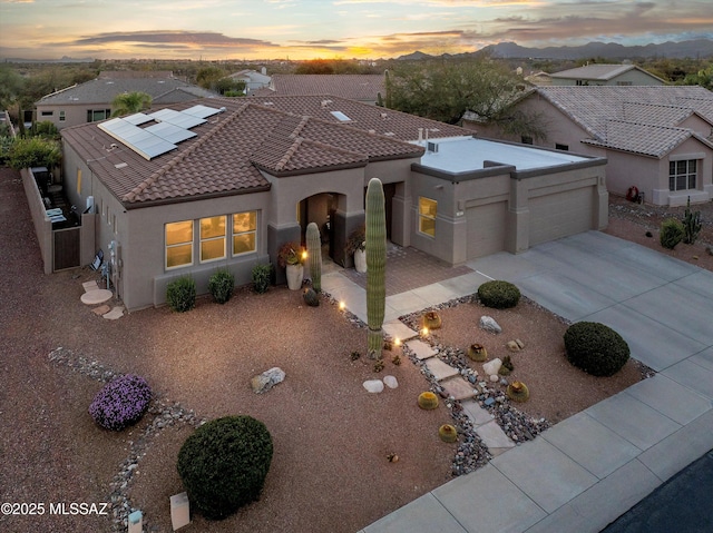 mediterranean / spanish home with solar panels, a tiled roof, concrete driveway, stucco siding, and an attached garage