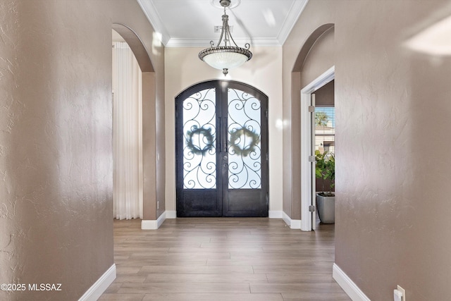 entrance foyer featuring wood finished floors, french doors, arched walkways, and ornamental molding