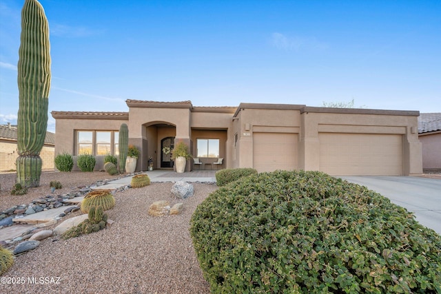 pueblo-style house featuring stucco siding, an attached garage, driveway, and a tile roof