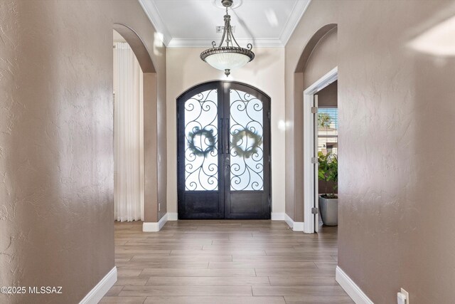foyer entrance featuring arched walkways, crown molding, french doors, and wood finished floors