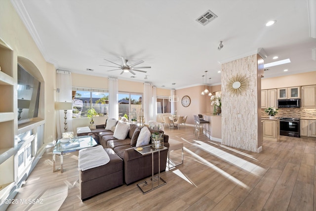 living area featuring ornamental molding, light wood-style flooring, visible vents, and ceiling fan