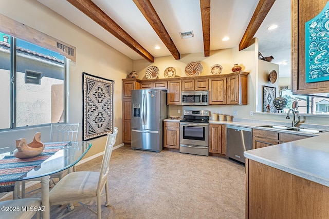 kitchen with beam ceiling, brown cabinets, stainless steel appliances, light countertops, and a sink