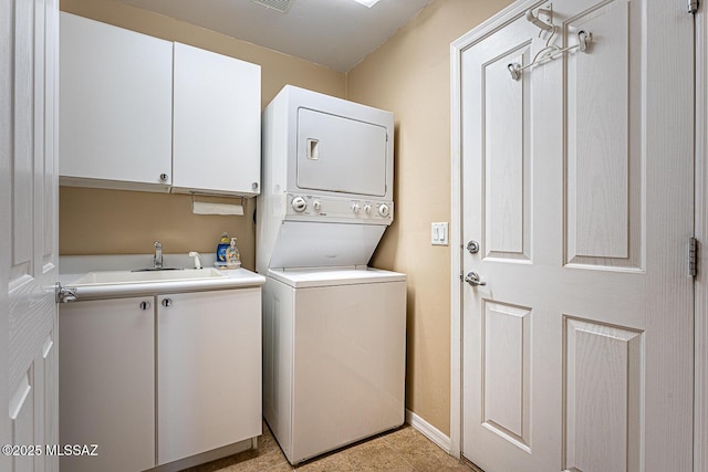 clothes washing area featuring cabinet space, baseboards, visible vents, stacked washing maching and dryer, and a sink