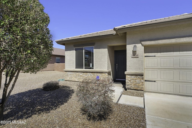 entrance to property with stucco siding, stone siding, fence, an attached garage, and a tiled roof