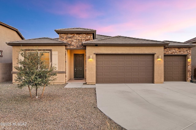 prairie-style house with an attached garage, stone siding, concrete driveway, and stucco siding