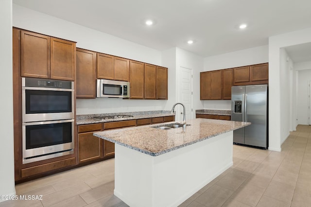 kitchen with recessed lighting, a sink, appliances with stainless steel finishes, light stone countertops, and an island with sink