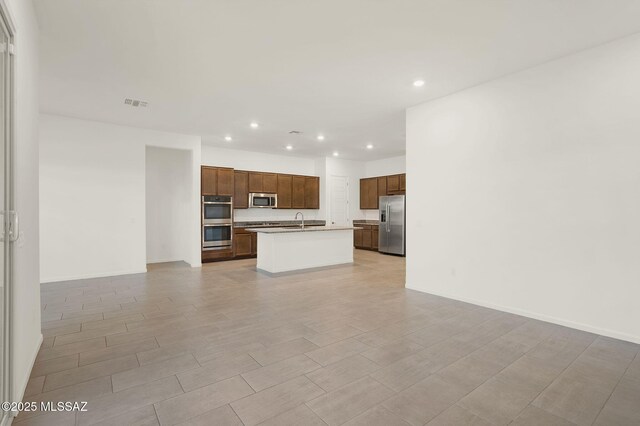 interior space featuring recessed lighting, a sink, open floor plan, appliances with stainless steel finishes, and an island with sink