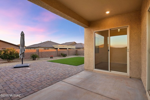 patio terrace at dusk featuring a fenced backyard and a yard
