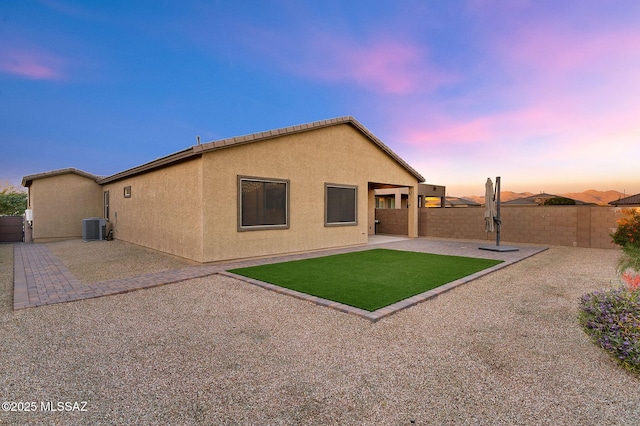 back of property with a yard, stucco siding, central AC, a patio area, and a fenced backyard