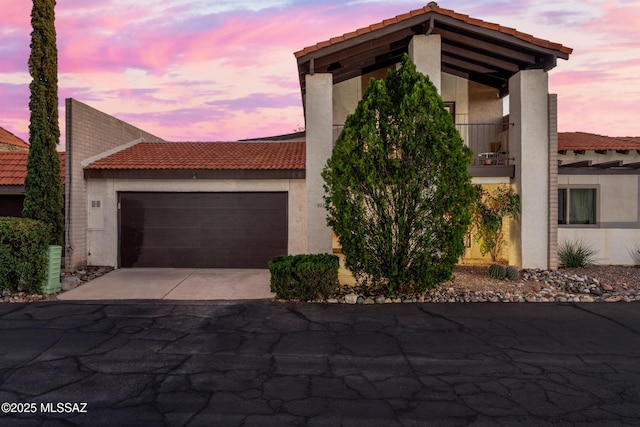 view of front of house with a tile roof, stucco siding, an attached garage, a balcony, and driveway