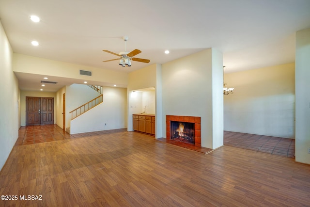 unfurnished living room with wood finished floors, stairway, a tile fireplace, and visible vents