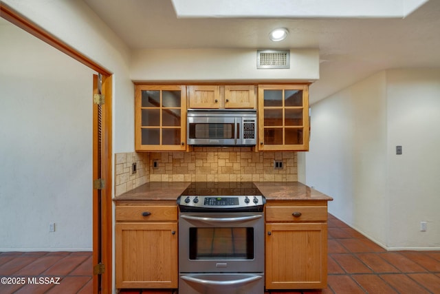 kitchen with stainless steel appliances, visible vents, glass insert cabinets, and backsplash