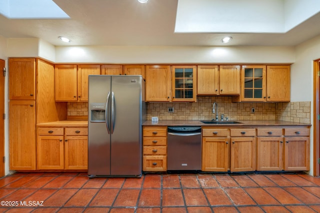 kitchen with dark tile patterned floors, a sink, appliances with stainless steel finishes, tasteful backsplash, and glass insert cabinets