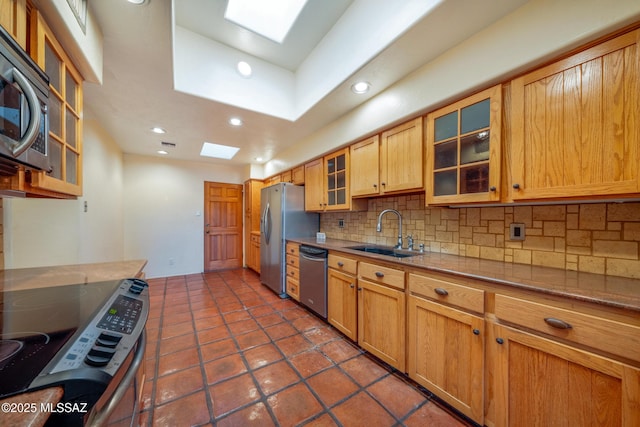 kitchen featuring a skylight, decorative backsplash, stainless steel appliances, and a sink