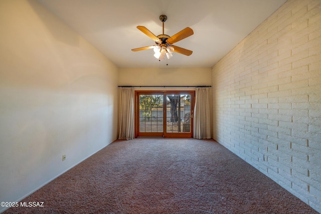 carpeted empty room featuring brick wall and a ceiling fan