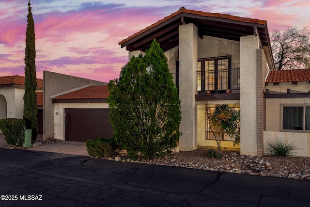 view of front facade with an attached garage, a balcony, concrete driveway, and stucco siding