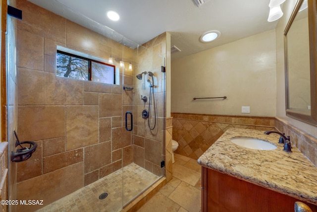 bathroom featuring a stall shower, stone tile floors, toilet, vanity, and tile walls