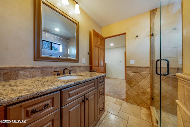 bathroom featuring a wainscoted wall, vanity, tile walls, a shower stall, and stone tile flooring