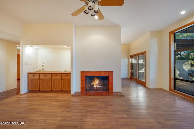 unfurnished living room with light wood-style flooring, ceiling fan, a sink, and a tile fireplace