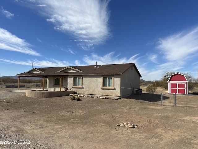 view of front of property featuring a patio, a storage unit, stucco siding, fence, and an outdoor structure