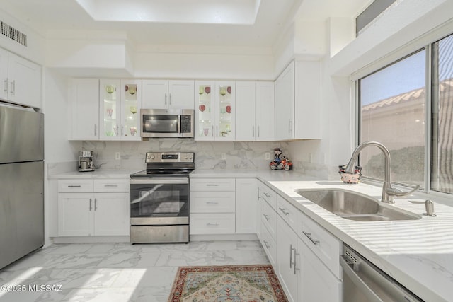 kitchen with appliances with stainless steel finishes, white cabinets, glass insert cabinets, and a sink