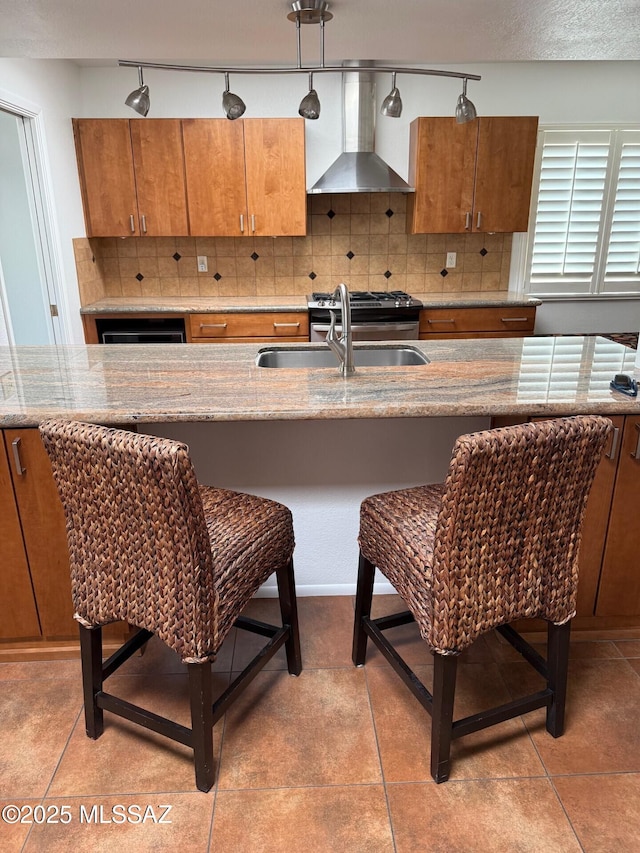 7471 E Serenity Ln, Tucson, AZ 85750 - kitchen with wall chimney exhaust hood, decorative backsplash, brown cabinetry, a sink, and light stone countertops