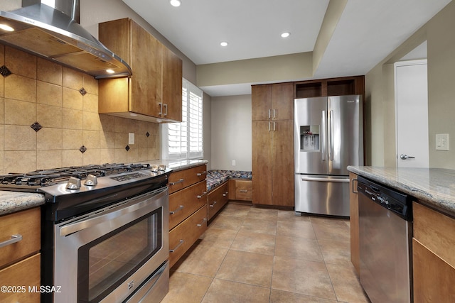 kitchen featuring brown cabinets, light stone countertops, wall chimney exhaust hood, and stainless steel appliances