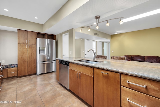 kitchen featuring appliances with stainless steel finishes, brown cabinetry, open floor plan, light tile patterned flooring, and a sink