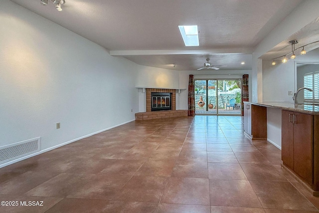 7471 E Serenity Ln, Tucson, AZ 85750 - unfurnished living room featuring a brick fireplace, a skylight, healthy amount of natural light, and baseboards