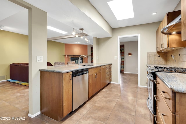 kitchen featuring tasteful backsplash, wall chimney exhaust hood, open floor plan, stainless steel appliances, and a sink