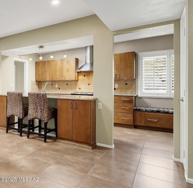 kitchen featuring a kitchen breakfast bar, light countertops, brown cabinets, wall chimney exhaust hood, and pendant lighting