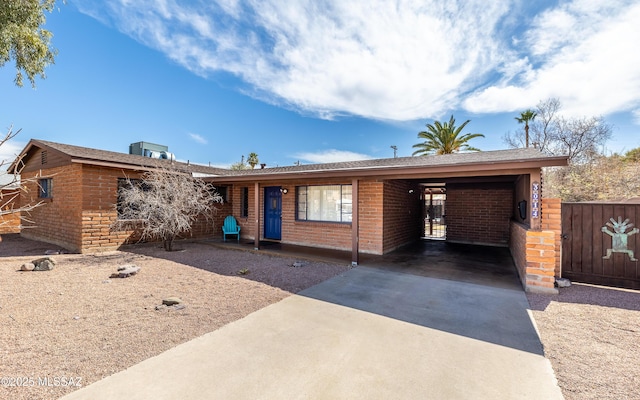 ranch-style house with a carport, concrete driveway, brick siding, and fence