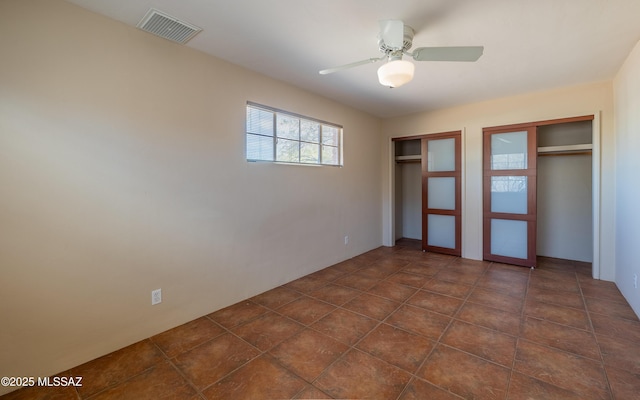 unfurnished bedroom with a ceiling fan, visible vents, and multiple closets