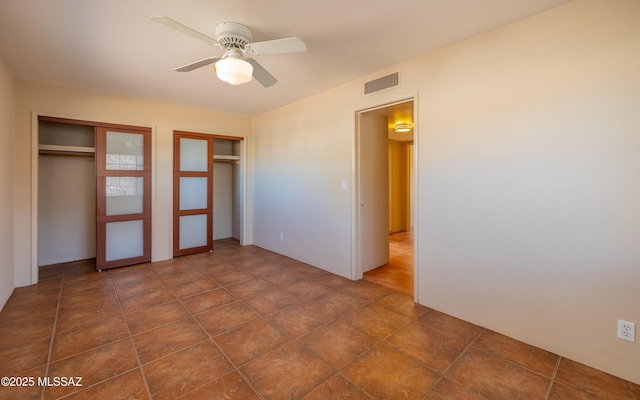 unfurnished bedroom with a ceiling fan, visible vents, and two closets