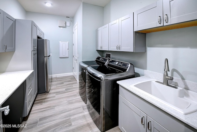 clothes washing area featuring washing machine and clothes dryer, cabinet space, light wood-style floors, a sink, and baseboards