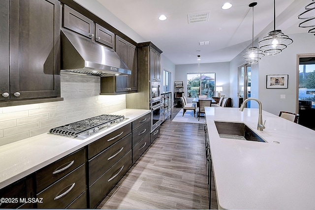 kitchen featuring under cabinet range hood, a sink, visible vents, dark brown cabinets, and appliances with stainless steel finishes