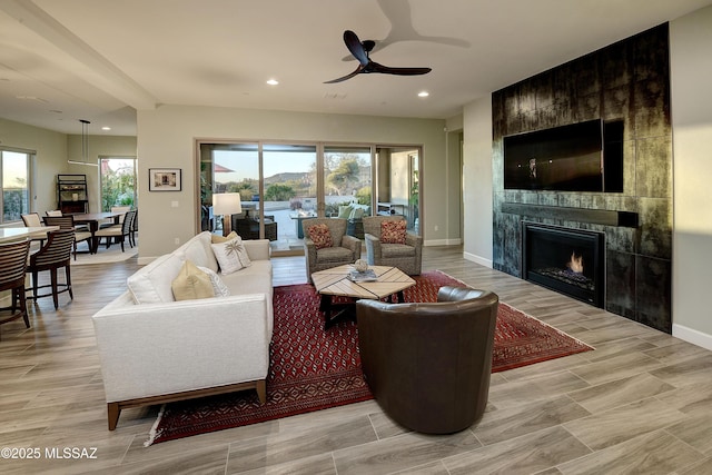 living room with light wood-style flooring, recessed lighting, a ceiling fan, baseboards, and a tiled fireplace