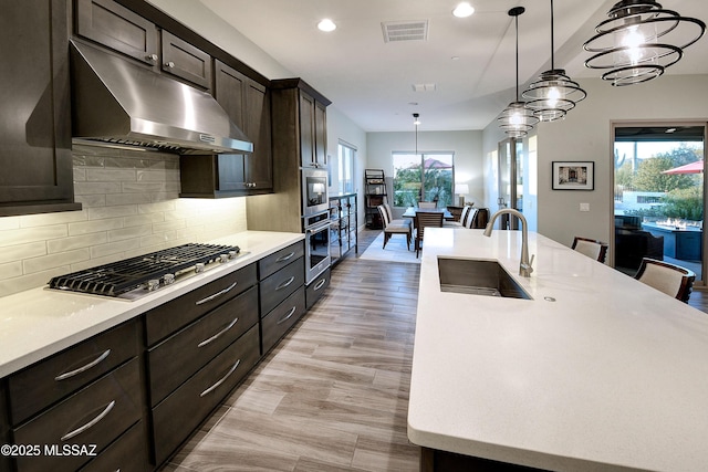 kitchen featuring under cabinet range hood, a sink, visible vents, light countertops, and appliances with stainless steel finishes