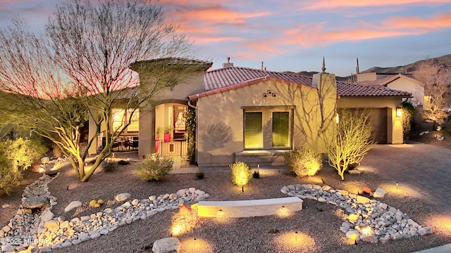 mediterranean / spanish house with driveway, a chimney, a tiled roof, an attached garage, and stucco siding