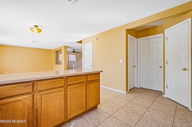 kitchen featuring light tile patterned floors, baseboards, brown cabinetry, ceiling fan, and light countertops