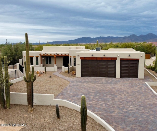 pueblo revival-style home featuring a garage, decorative driveway, a mountain view, and stucco siding