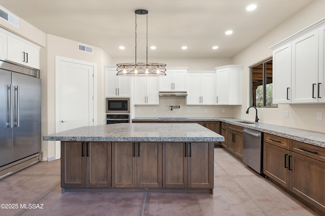 kitchen featuring visible vents, white cabinetry, a sink, built in appliances, and under cabinet range hood