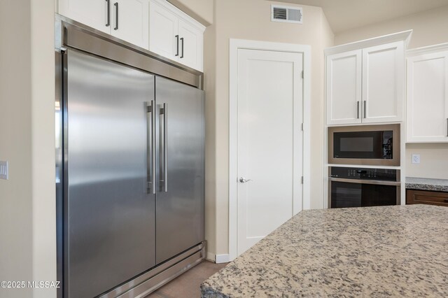 kitchen with built in appliances, light stone counters, visible vents, and white cabinetry